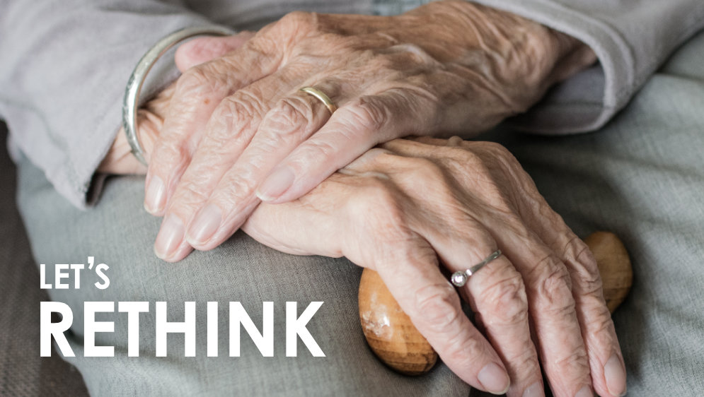 An old person's hands resting on a cane