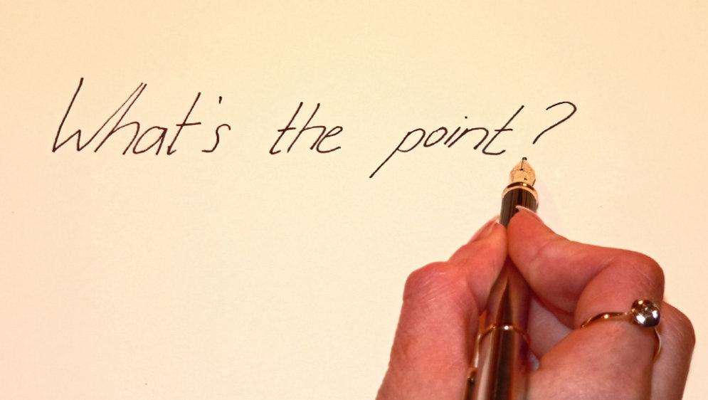 A hand holding a pen, writing the words, "What's the Point?".